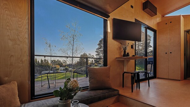 A modern interior with a large window, a sofa, a small table, and a flat-screen TV mounted on the wall.