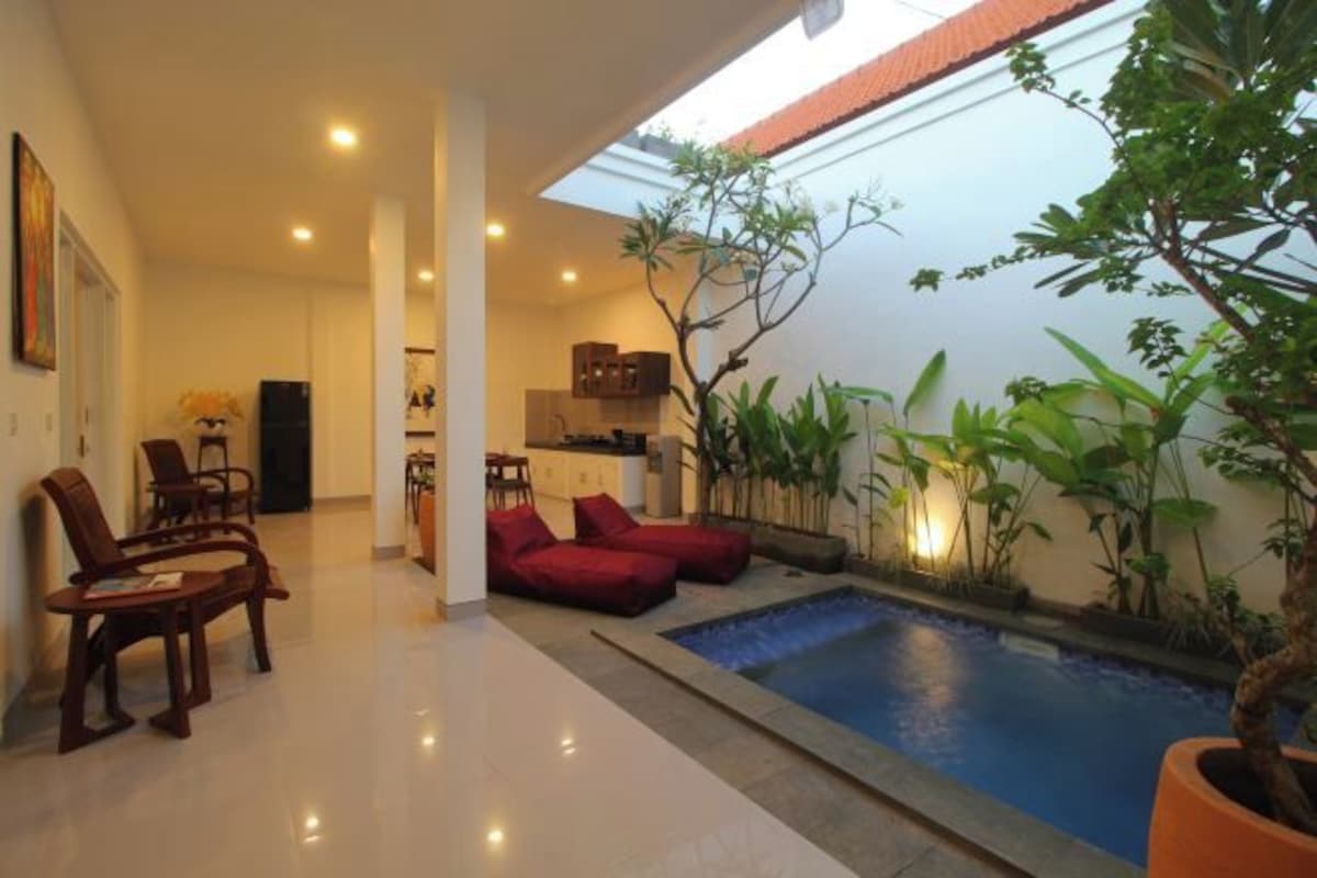 Un interior moderno con piscina, zona de estar y cocina al fondo.