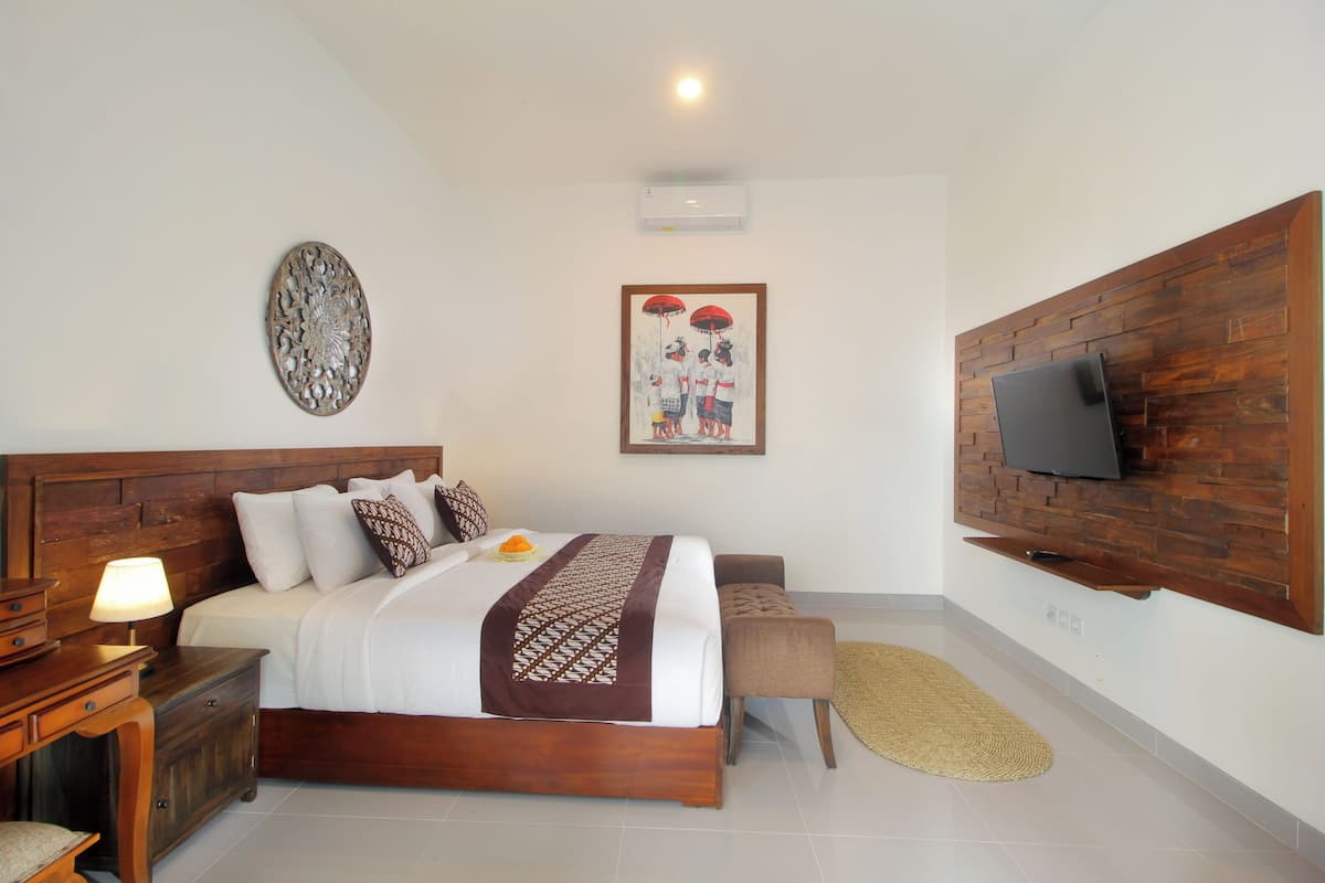 Camera da letto con testiera in legno, letto con biancheria da letto bianca e copriletto fantasia, comodino con lampada, televisore a schermo piatto montato su pannello in legno e decorazione a parete.