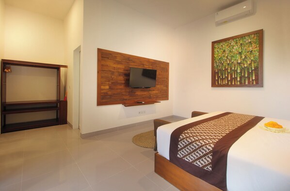 A hotel room with a bed, a television mounted on a wooden panel, a painting on the wall, and a small round rug.