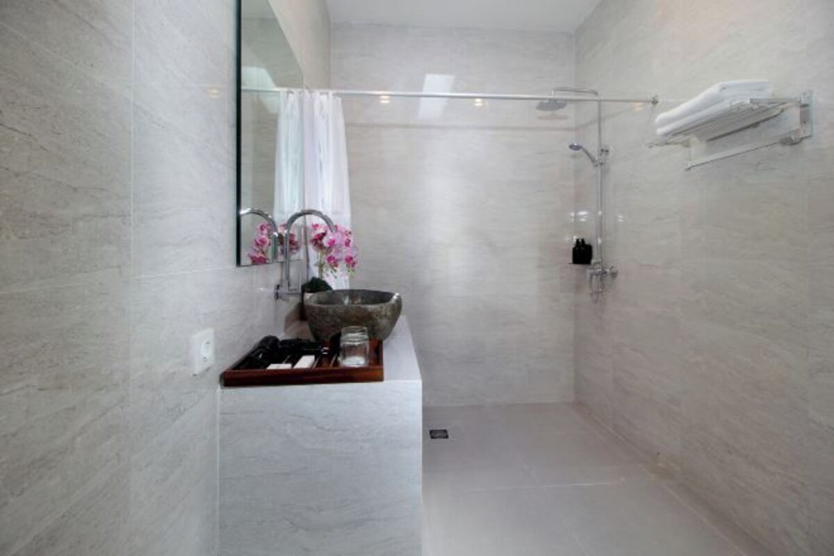 A modern bathroom with a stone sink, a mirror, a shower, and a towel rack.