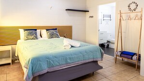 Ένα στρωμένο κρεβάτι με προσοχή, με ένα μπλε και λευκό κλινοσκεπάσμα, ένα ξύλινο προσκέφαλο και ένα λευκό κομοδίνο στα αριστερά.