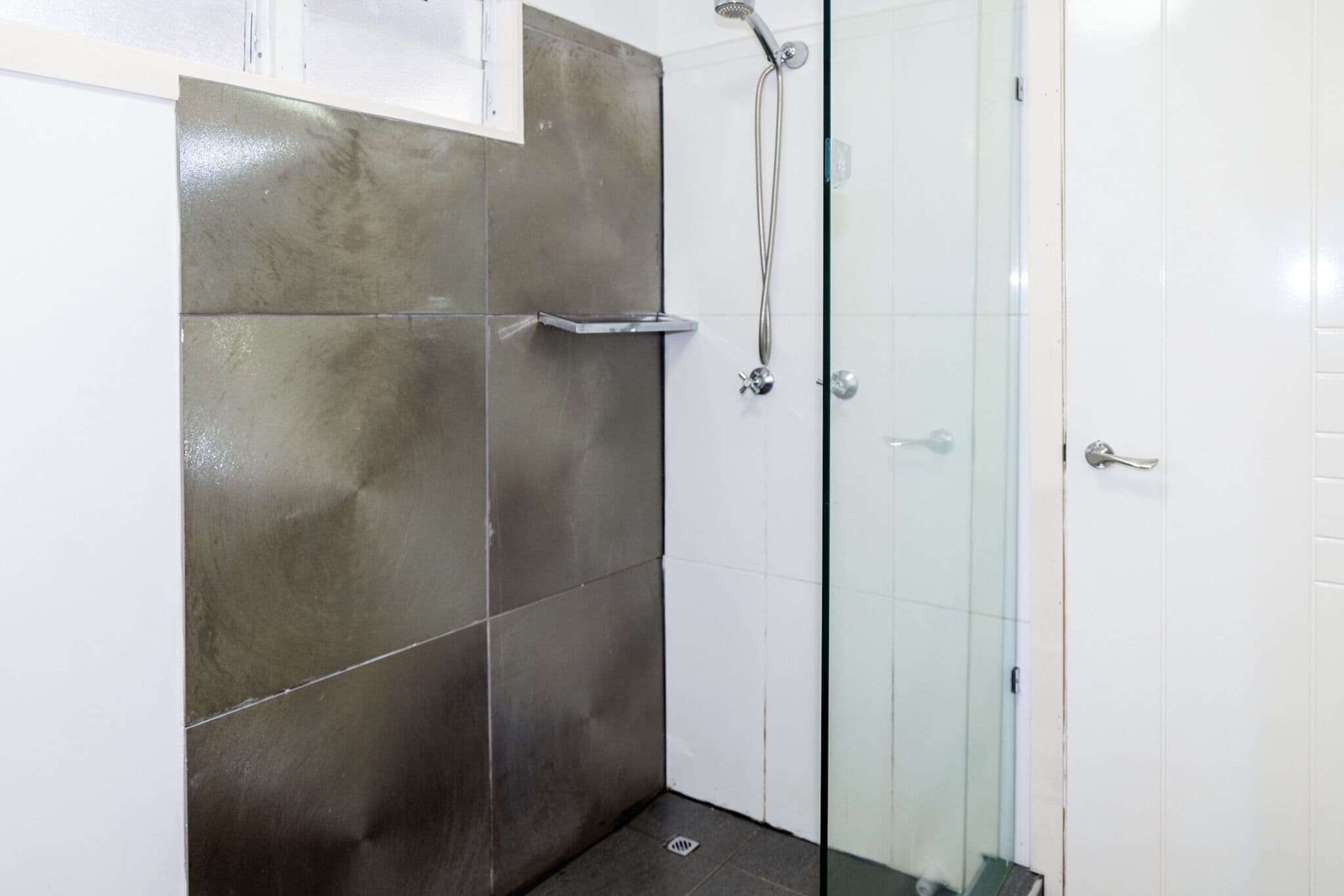 Una ducha con puerta de cristal y estante de metal.