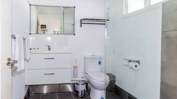 Um banheiro moderno com pia branca, espelho, vaso sanitário e chuveiro.