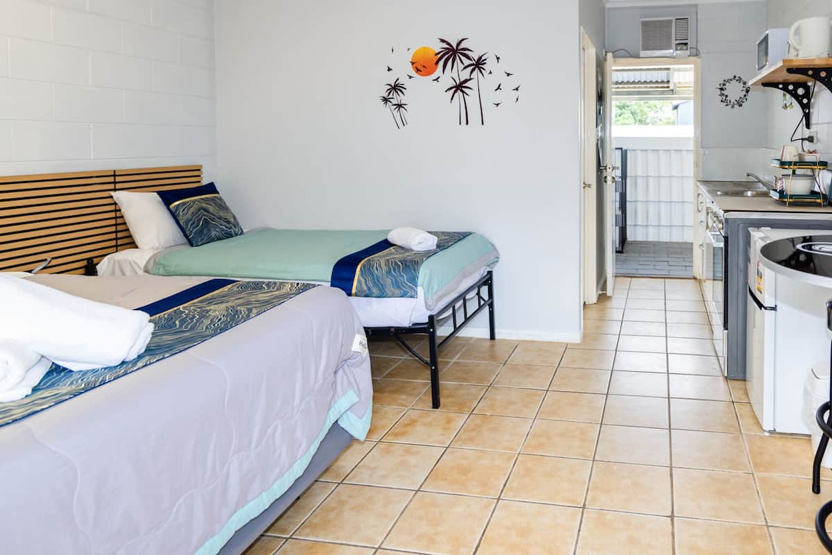 A bedroom with two beds, a kitchenette, and a bathroom visible through an open door.
