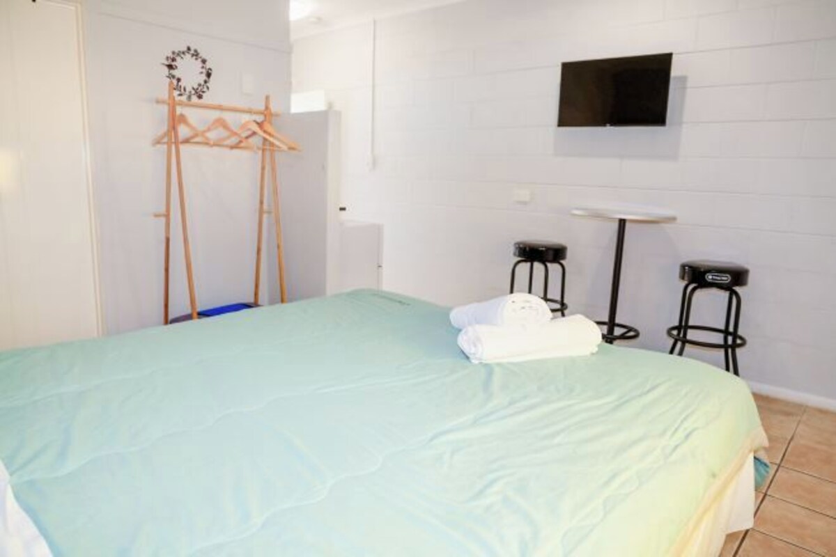 Ein Hotelzimmer mit einem Bett, einem an der Wand befestigten Fernseher und zwei Barhocker.