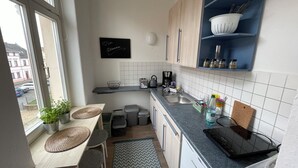 A compact kitchen with a window, a small dining area, and a blue shelf with kitchen utensils. - Studio11 (Torgau)