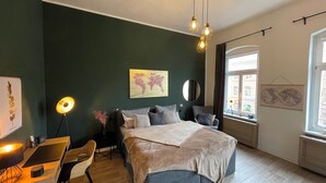 A bedroom with a bed, bedside table, lamp, chair, and a view of the city through a window. - Studio11 (Torgau)