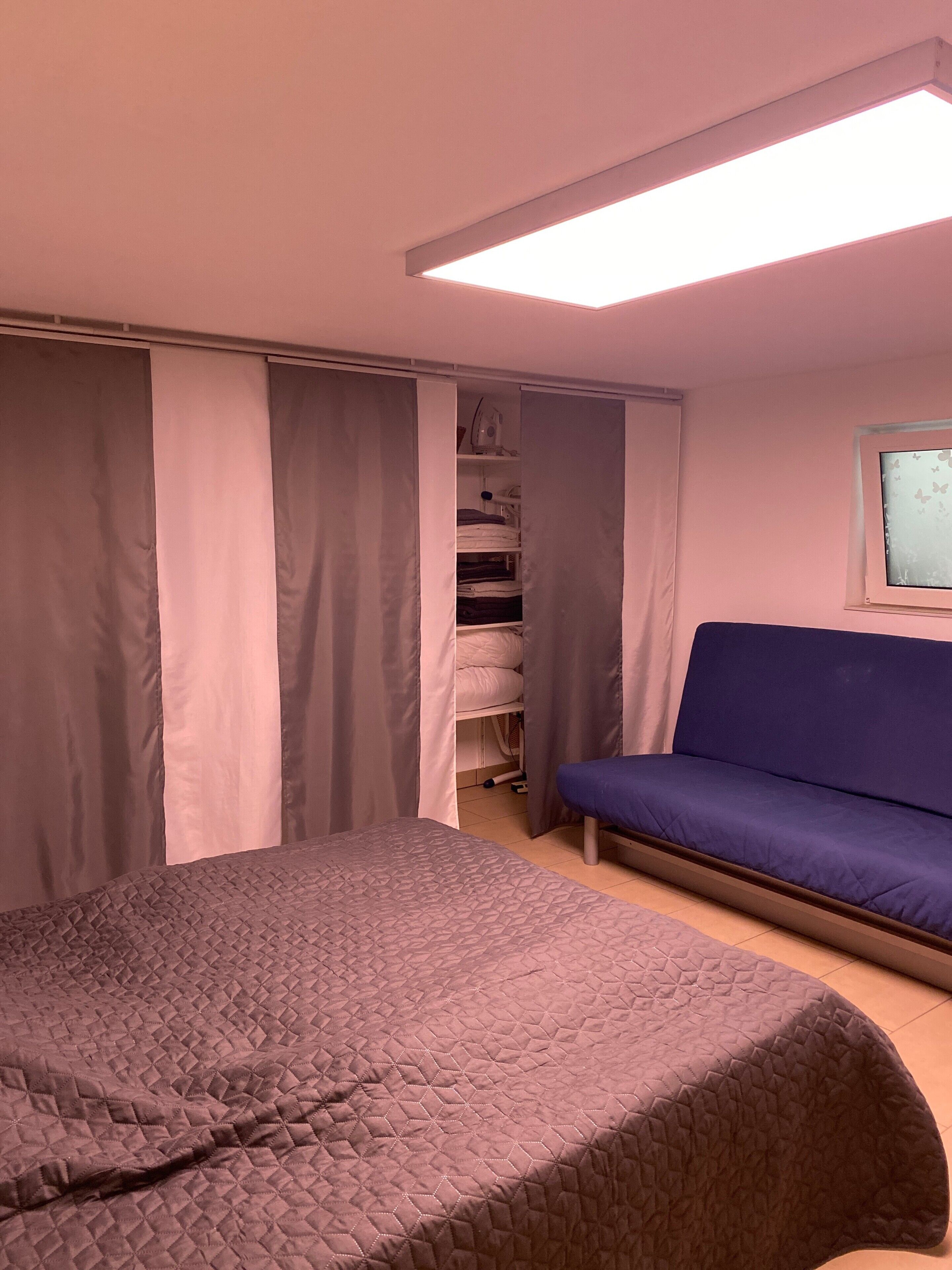 A bedroom with a bed, a blue sofa, a wardrobe, and a window with a butterfly design.