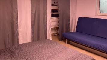 A bedroom with a bed, a blue sofa, a wardrobe, and a window with a butterfly design.