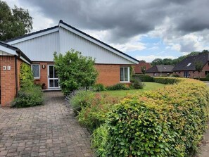 A single-story building with a brick facade, a flat roof, and a paved driveway leading to a gated entrance. - Holiday Home 'Ferienhaus Sprante' with Private Terrace, Private Garden and Wi-Fi (Brunsbüttel)