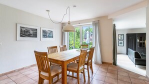 A dining area with a wooden table and chairs, a pendant light, and large windows with curtains. - Holiday Home 'Ferienhaus Sprante' with Private Terrace, Private Garden and Wi-Fi (Brunsbüttel)