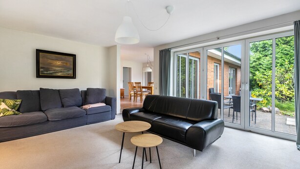 A modern living room with a black leather sofa, a grey sofa, and two round wooden tables. - Holiday Home 'Ferienhaus Sprante' with Private Terrace, Private Garden and Wi-Fi (Brunsbüttel)