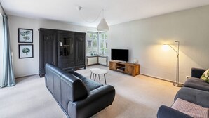 A living room with a black leather sofa, a television, a wooden cabinet, and a floor lamp. - Holiday Home 'Ferienhaus Sprante' with Private Terrace, Private Garden and Wi-Fi (Brunsbüttel)