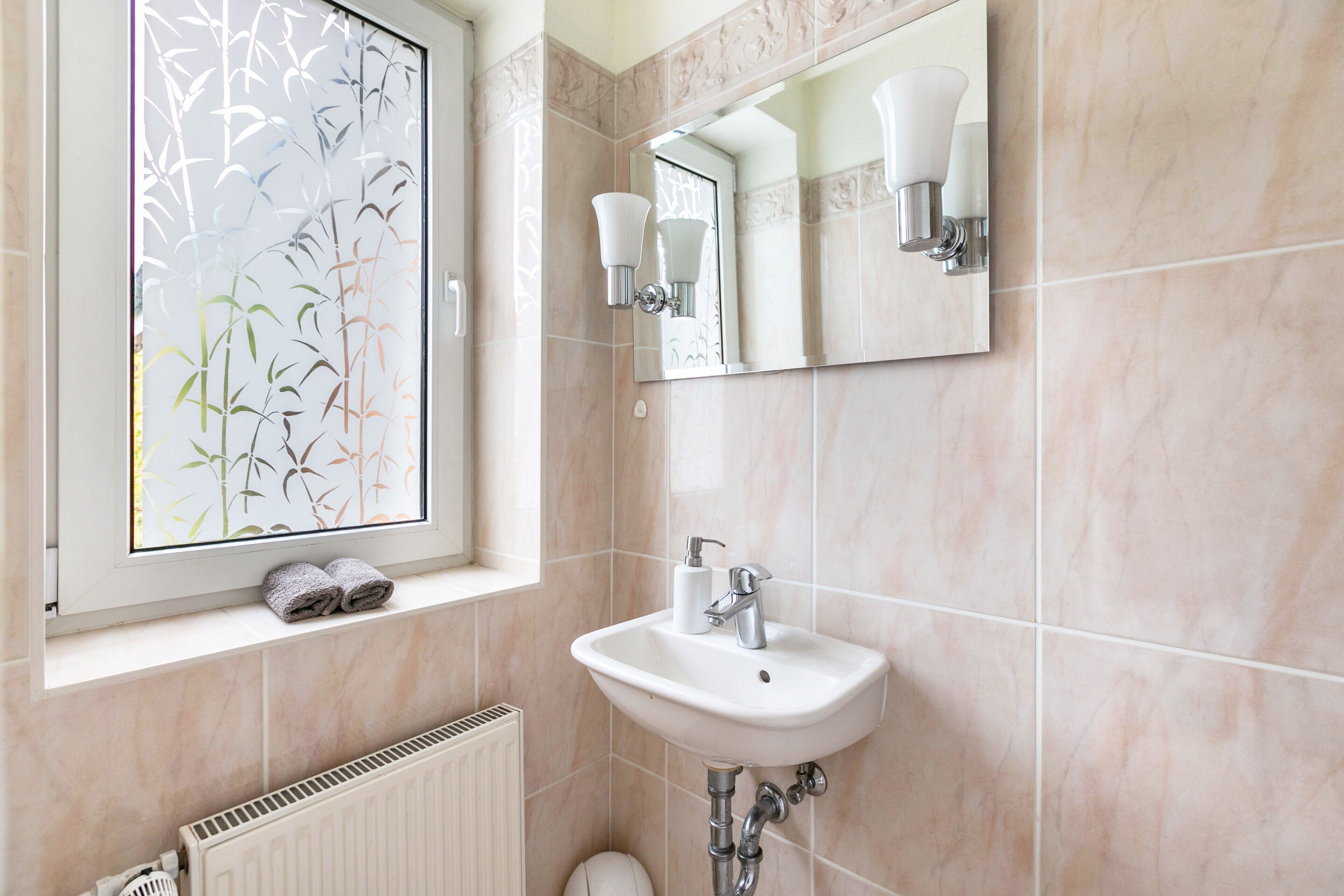 Une salle de bain avec une fenêtre, un lavabo, un miroir et des toilettes.