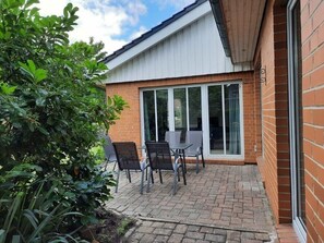 A patio with a table and chairs, a brick wall, and a glass door. - Holiday Home 'Ferienhaus Sprante' with Private Terrace, Private Garden and Wi-Fi (Brunsbüttel)
