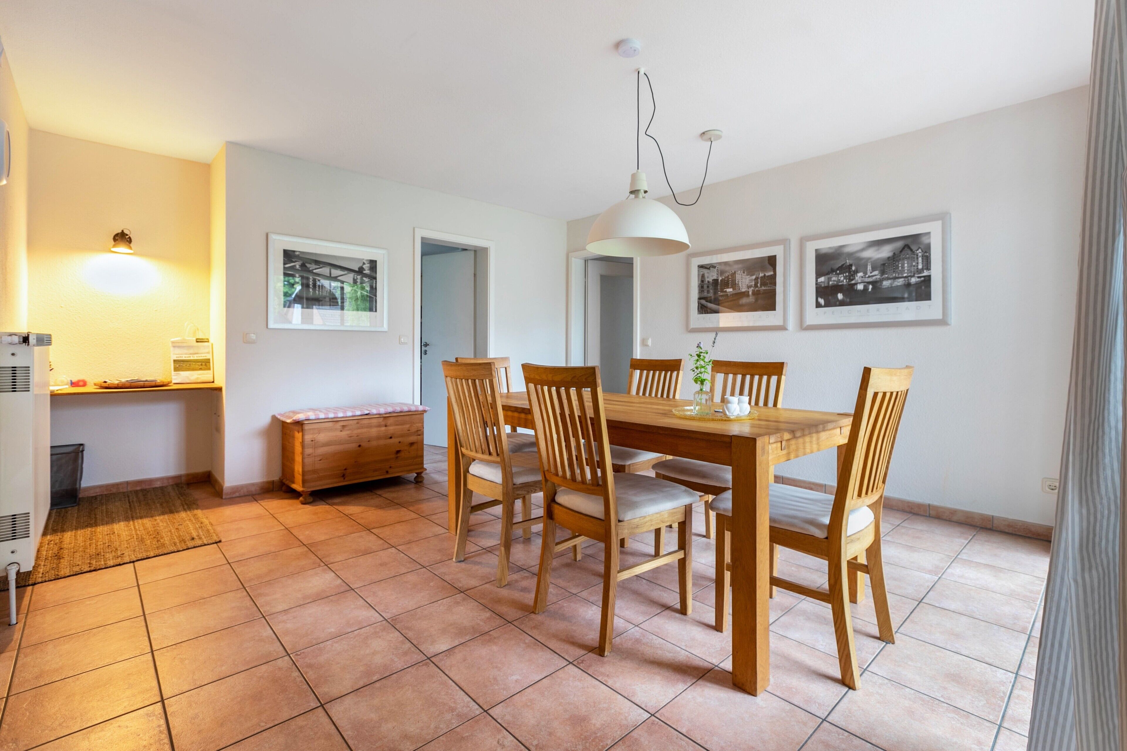 Een eethoek met een houten tafel en stoelen, een bank, een wandlamp en ingelijste foto's.
