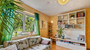 Een moderne woonkamer met een bank, een boekenkast en grote ramen.