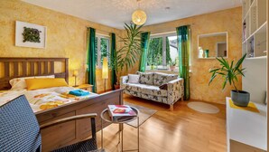 Een kamer met een bed, een bank, een kleine tafel, een stoel, een potplant en een spiegel aan de muur.