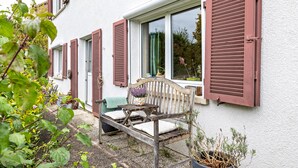 Een houten bank voor een huis met luiken, een raam en potplanten.