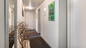 Een gang met een tapijtvloer, een deur aan het einde en een schilderij aan de muur.