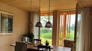 A dining area with a wooden table, chairs, hanging lamps, and a view of greenery outside. - Apartment 'Am Stadtwald' with Mountain View, Private Terrace and Wi-Fi (Triberg)