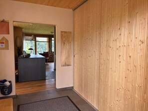 Een modern interieur met een wand van houten panelen, een keuken met een centraal eiland en een uitzicht door een deur.