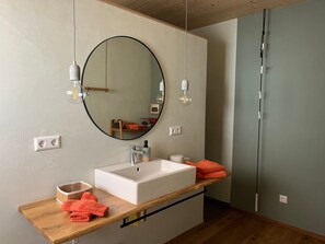 Een moderne badkamer met een ronde spiegel, een wit wastafelmeubel en een houten aanrechtblad, met twee hanglampen.