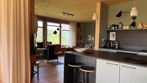 A modern kitchen with wooden flooring, a central island with stools, pendant lighting, and a view of the outdoors. - Apartment 'Am Stadtwald' with Mountain View, Private Terrace and Wi-Fi (Triberg)