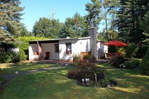 A single-story house with a chimney, a red umbrella, and a garden with a small pond.