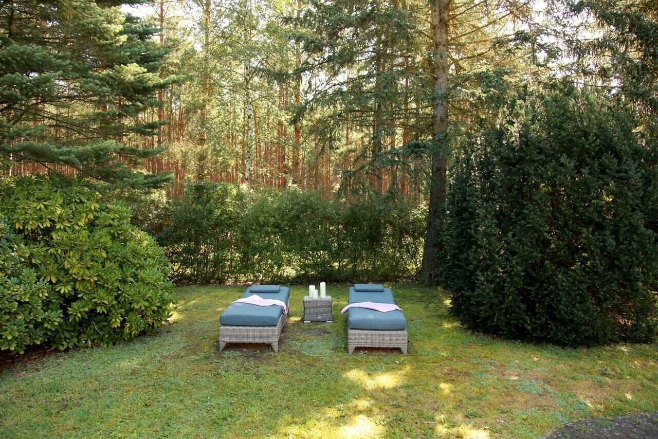Et fredfyldt udendørs område med to fletstuletage, et lille bord og en bænk, omgivet af frodig vegetation og høje træer.
