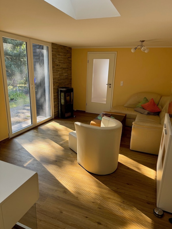 A modern living room with a large sliding glass door, a stone accent wall, a white sofa with colorful cushions, and a wooden floor.