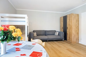 A room with a bunk bed, a gray sofa, a wooden wardrobe, and a table with a floral tablecloth. - Apartment in 'St. Pauli' Hotel with Wi-Fi (Hamburg)