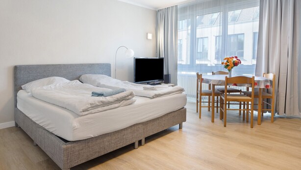 A hotel room with a bed, a desk, a chair, a TV, and a window with curtains. - Apartment in 'St. Pauli' Hotel with Wi-Fi (Hamburg)