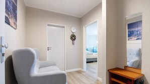 A modern room with a grey armchair, a wooden shelf, a wall clock, and a door leading to another room. - Apartment in 'St. Pauli' Hotel with Wi-Fi (Hamburg)