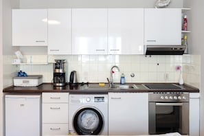 A compact kitchen with white cabinets, a built-in washing machine, a coffee maker, and a small oven. - Apartment in 'St. Pauli' Hotel with Wi-Fi (Hamburg)