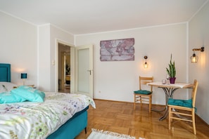 A bedroom with a bed, a desk, chairs, a plant, and a world map on the wall.