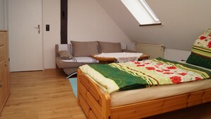 Une chambre avec un plafond en pente, un lit en bois, un canapé, une petite table et un radiateur.