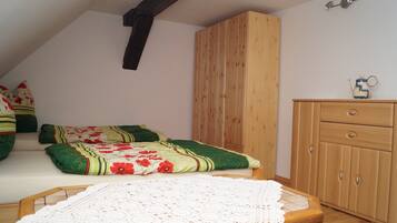 A room with a sloped ceiling, a wooden wardrobe, a bed with floral bedding, and a small table with a white lace tablecloth.