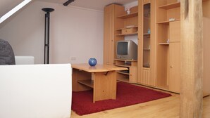 Une pièce avec un plafond en pente, un bureau en bois surmonté d’un tapis rouge, une télévision et des armoires en bois.