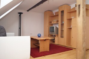 A room with a sloped ceiling, a wooden desk with a red rug, a television, and wooden cabinets.
