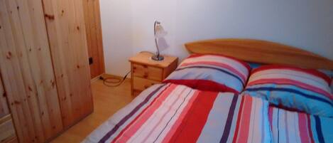 Un dormitorio con un armario de madera, una mesita de noche con lámpara y una cama con ropa de cama a rayas.