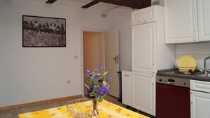 Une cuisine avec des meubles blancs, un plafond en bois, une table à manger ornée d’un vase de fleurs et une photographie en noir et blanc accrochée au mur.