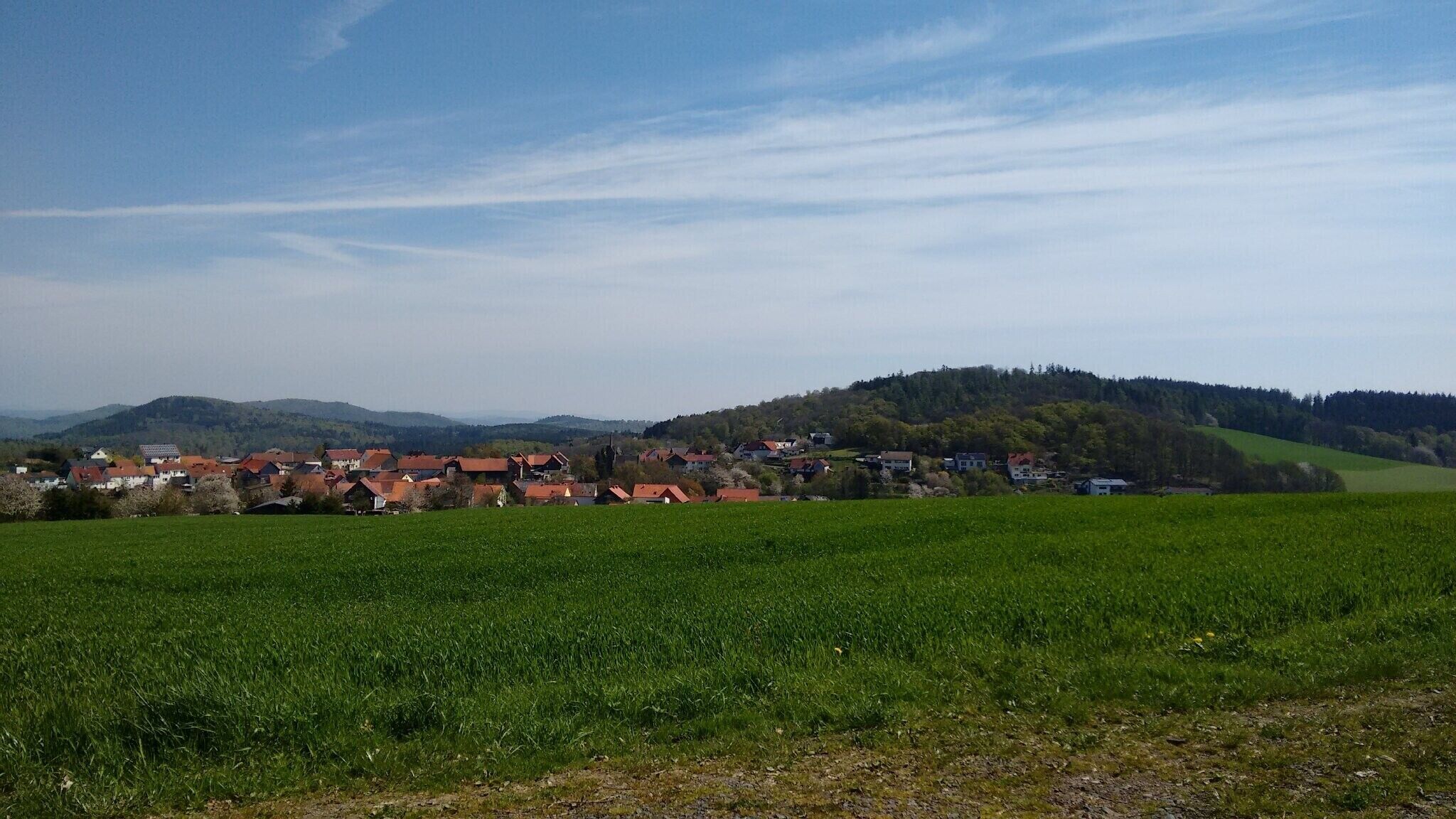 A rural landscape with a village, green fields, and hills in the background.