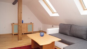 Une pièce de style loft avec un plafond en pente, une table en bois, un canapé gris et un meuble avec des portes en verre.