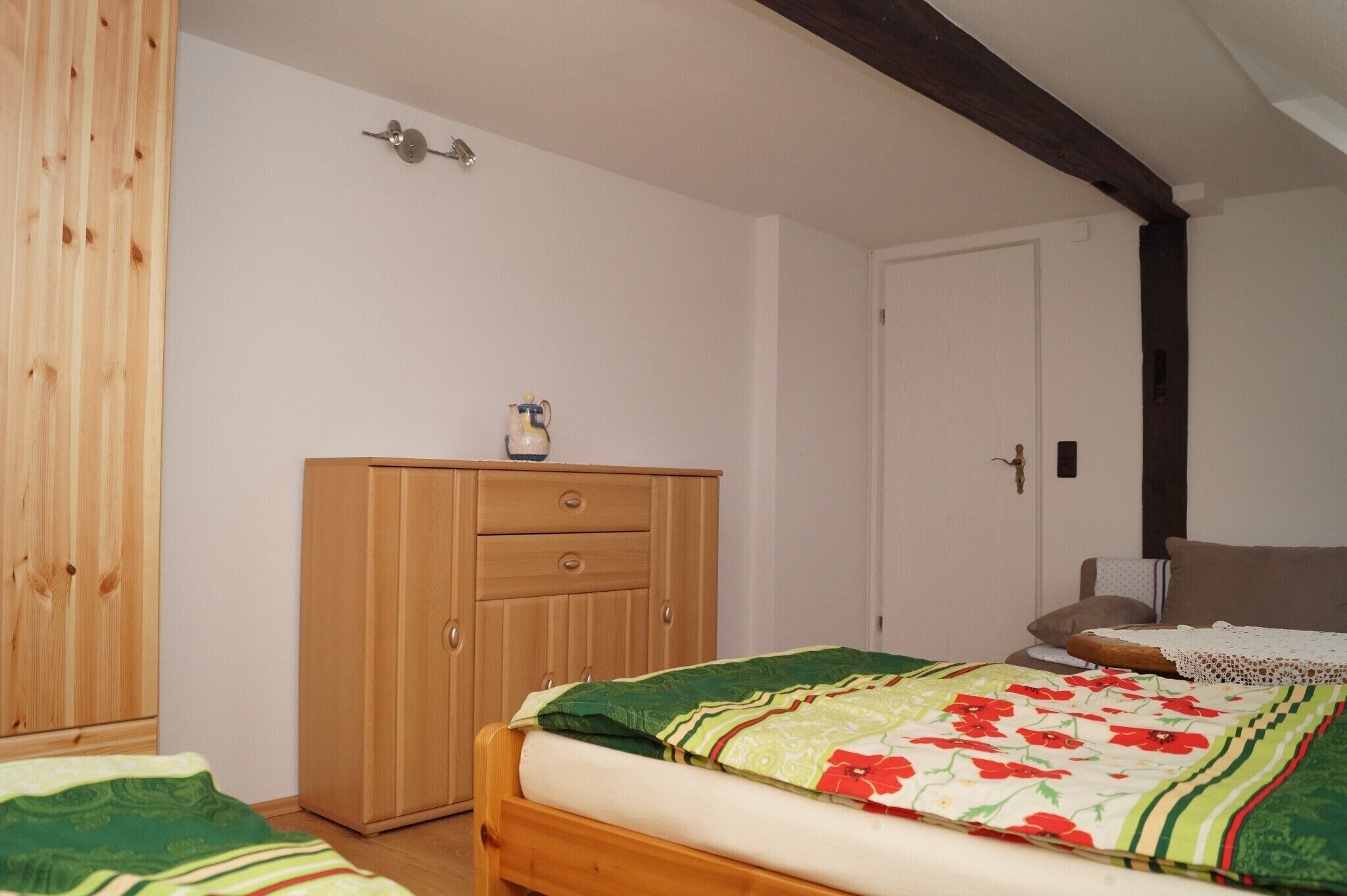 Une chambre avec une armoire en bois, un lit recouvert d’une couvre-lit à motifs floraux et une porte blanche.