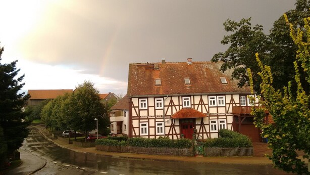 Un bâtiment traditionnel à colombages, doté d’un toit à pignon, entouré d’arbres et bordé d’une rue pavée.