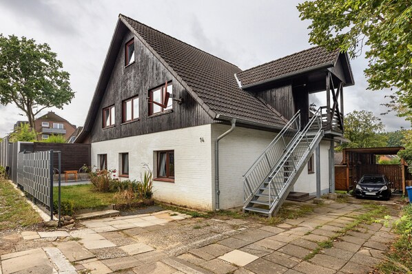 Een twee verdiepingen tellend huis met een steil dak, een trap en een auto op de oprit.