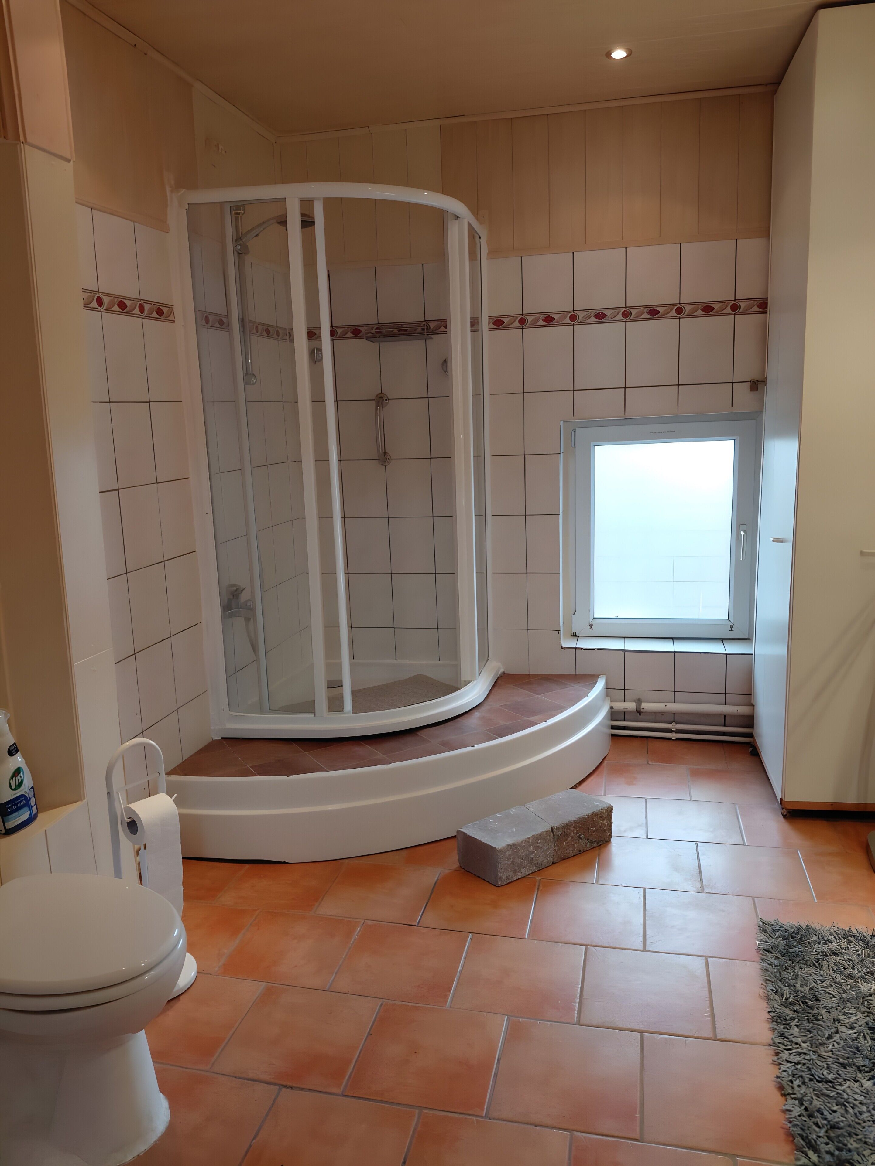 Ein Badezimmer mit Dusche, Toilette und Fenster.