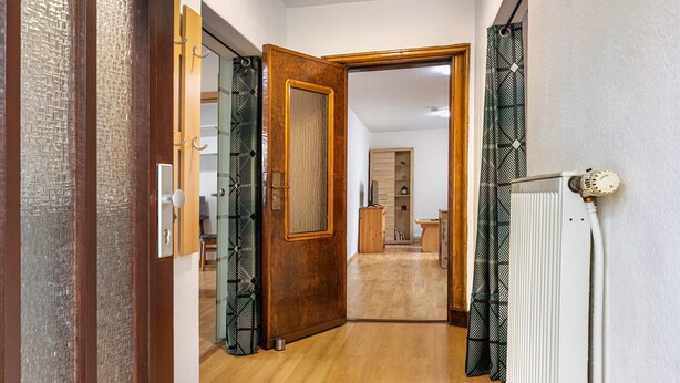 A hallway with a wooden door, a radiator, and patterned curtains. - Apartment 'Buchholz I D N' with Private Terrace, Shared Garden and Wi-Fi (Buchholz in der Nordheide)